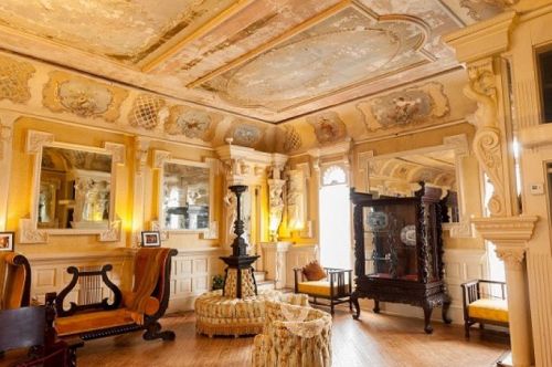Elegant vintage room with ornate ceilings, mirrors, and antique furniture, featuring a cozy seating area.