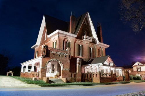 A large, historic brick mansion with intricate architectural details, illuminated at night against a dark sky.