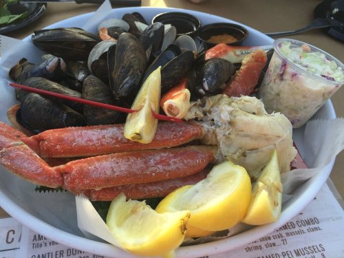 A seafood platter featuring crab legs, mussels, shrimp, lemon wedges, and a side of coleslaw.