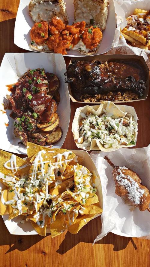 A variety of delicious dishes including nachos, tacos, BBQ, and a corn dog, arranged on a wooden table.