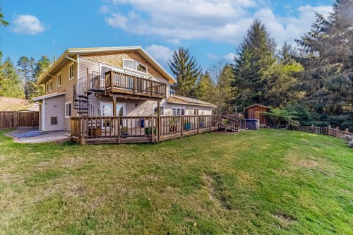 A spacious two-story house with a wooden deck, surrounded by trees and a grassy yard under a blue sky.