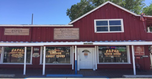 Red wooden building with signs for "Papa's Ranch House Restaurant" and "Saloon Ghost Tours" on a sunny day.