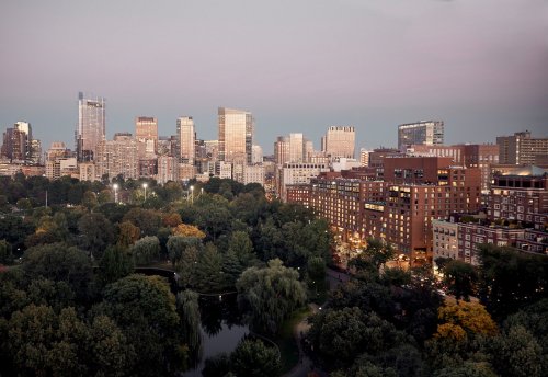 City skyline at dusk, featuring modern buildings and lush green parks with a tranquil pond.