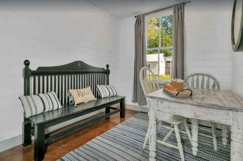 Cozy room with a black bench, a wooden table, and a window overlooking a garden, featuring a striped rug.
