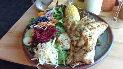 Grilled fish served with a colorful salad, corn, and assorted vegetables on a rustic plate.