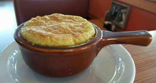 A golden, fluffy soufflé served in a brown ceramic dish on a white plate.