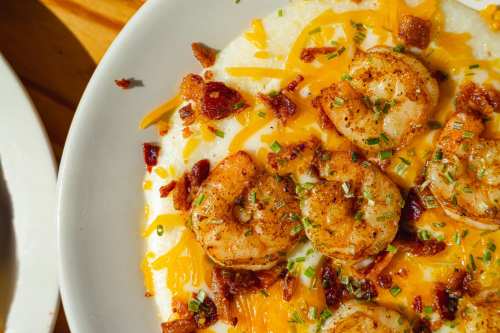 A close-up of creamy grits topped with seasoned shrimp, cheddar cheese, crispy bacon, and fresh chives.