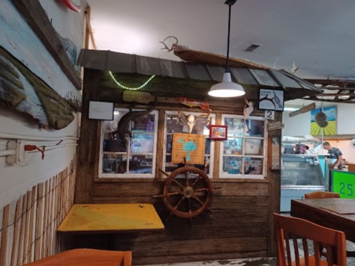 A rustic wooden shack with a ship's wheel, fish decor, and a cozy dining area in a seafood restaurant.