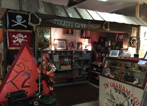 A whimsical pirate-themed shop entrance with decorations, a pirate statue, and various merchandise on display.