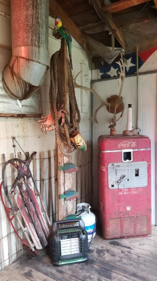 A rustic interior featuring a vintage Coca-Cola cooler, ropes, antlers, and a colorful parrot decoration.