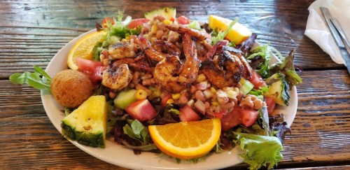 A vibrant salad topped with grilled shrimp, corn, tomatoes, and citrus, served with a side of cornbread.