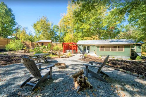 A cozy outdoor space with two chairs, a fire pit, and a path surrounded by trees and greenery.
