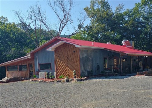 A modern building with a red roof, wooden accents, and a gravel driveway, surrounded by trees and landscaping.