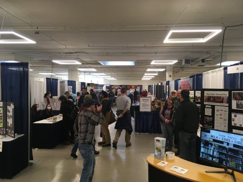 A busy exhibition hall with booths and attendees engaging in conversations and viewing displays.