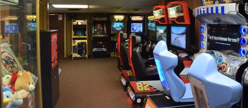 A retro arcade room featuring various gaming machines, including racing and shooting games, with colorful cabinets.