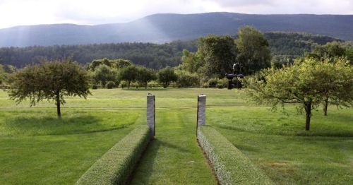 A serene landscape featuring manicured grass paths, trees, and distant mountains under a cloudy sky.