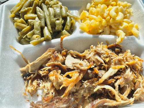 A styrofoam food container with pulled pork, green beans, and macaroni and cheese.