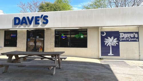 Exterior of Dave's Grill & Grocery with a picnic table outside and signs for Pepsi and a palm tree logo.