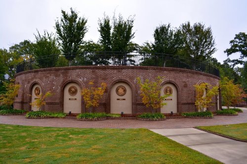 A circular brick structure with decorative plaques, surrounded by trees and greenery, on a cloudy day.