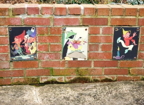 Three colorful cartoon panels mounted on a brick wall, featuring whimsical characters in playful poses.