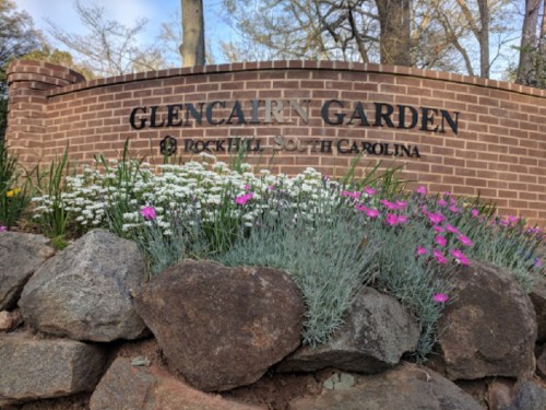 Sign for Glencairn Garden in Rock Hill, South Carolina, surrounded by colorful flowers and a stone wall.