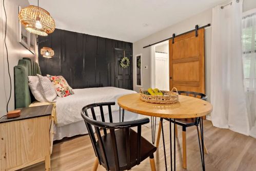 Cozy bedroom with a bed, wooden sliding door, and a small dining table with chairs, decorated with plants and warm lighting.