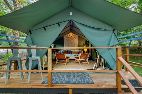 A cozy glamping tent with a wooden deck, featuring seating and decor, surrounded by trees.