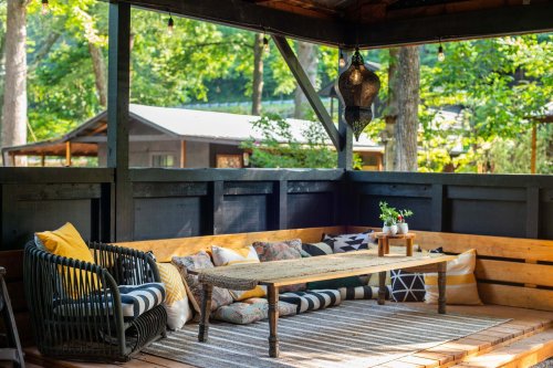 Cozy outdoor seating area with a wooden table, cushions, and greenery in a serene, shaded environment.