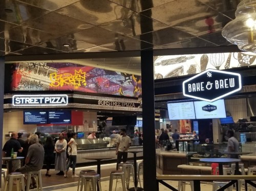 A bustling food court featuring "Street Pizza" and "Bake & Brew" with colorful graffiti art in the background.