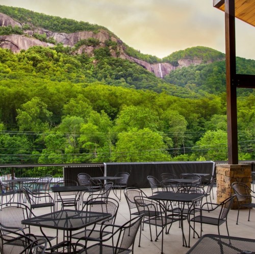 A scenic view of lush green mountains under a cloudy sky, with outdoor seating in the foreground.