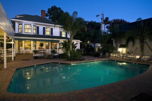 A serene backyard at dusk featuring a pool, palm trees, and a charming house with warm lights.
