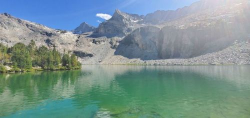 A serene lake surrounded by mountains, with clear blue water reflecting the landscape under a bright sky.