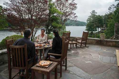 A group dining outdoors by a lake, enjoying food and drinks with trees and water in the background.