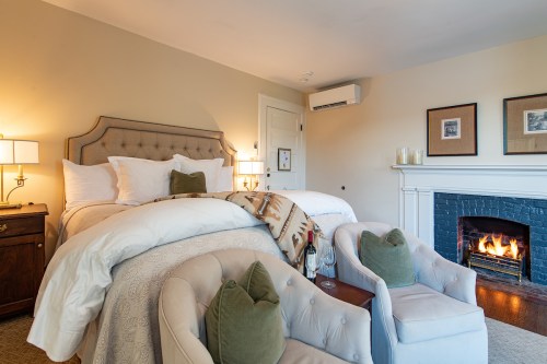 Cozy bedroom with a plush bed, armchairs, and a fireplace, creating a warm and inviting atmosphere.