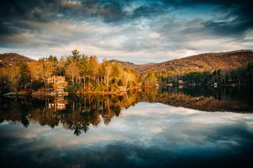 A serene lake surrounded by trees and mountains, reflecting the colorful sky and landscape at sunset.