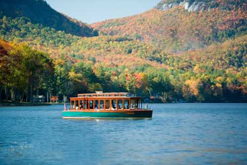 A wooden boat glides across a lake surrounded by vibrant autumn foliage and mountains in the background.