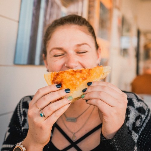 A person smiles while holding a cheesy, golden-brown quesadilla, ready to take a bite.