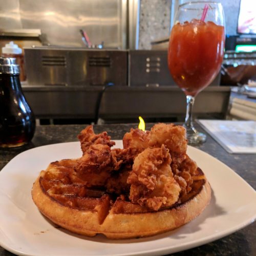 A plate of crispy fried chicken on a golden waffle, accompanied by a drink in a glass.