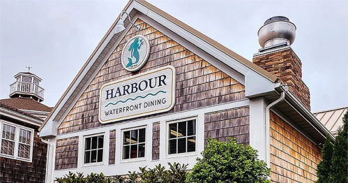 Exterior of a waterfront dining restaurant named "Harbour," featuring wooden shingles and a decorative sign.