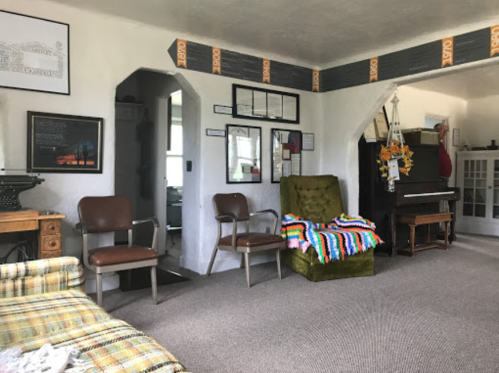 A cozy living room with a green chair, colorful blanket, piano, and framed pictures on the walls.