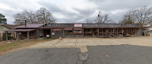 A rustic wooden building with a metal roof, decorated with lights and signs, set against a cloudy sky.