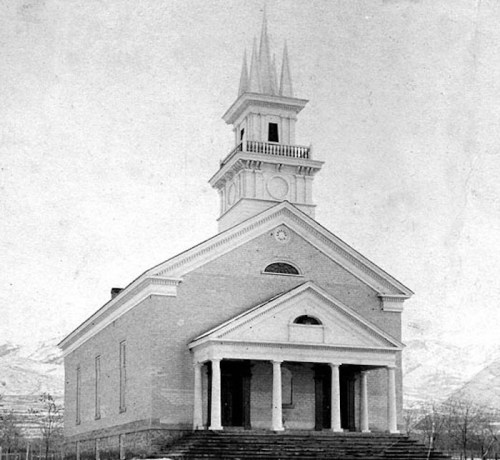 Historic church building with a tall spire, columns, and a mountainous backdrop, captured in black and white.