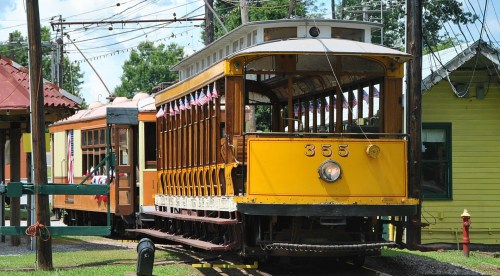 A vintage yellow streetcar with decorative flags parked beside a wooden station in a sunny setting.
