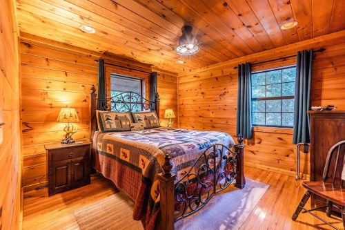 Cozy wooden bedroom with a quilted bed, two lamps, and a window, featuring warm tones and rustic decor.