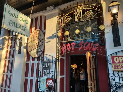 Exterior of Hop Sing Palace, featuring red and white decor, lanterns, and an open door inviting customers inside.