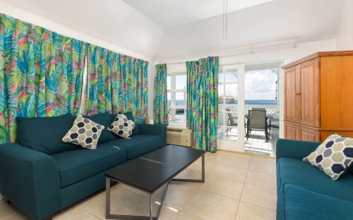 Bright living room with tropical-patterned curtains, teal sofas, a coffee table, and a view of the outdoors.