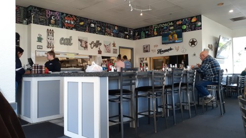 A cozy diner interior with a counter, patrons seated, and staff serving food in a colorful, welcoming atmosphere.