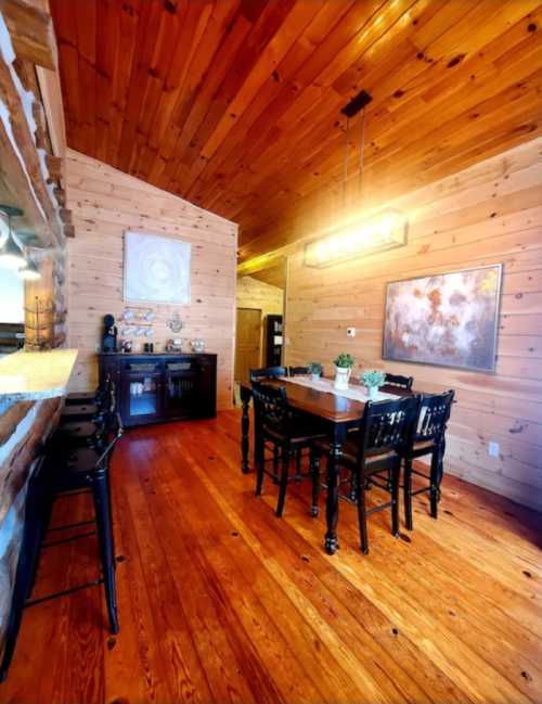 Cozy dining area with wooden walls, a table, black chairs, and warm lighting in a rustic setting.