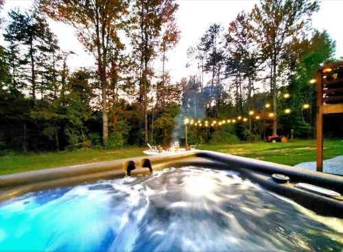 A hot tub with bubbling water, surrounded by trees and string lights, set in a serene outdoor landscape at dusk.