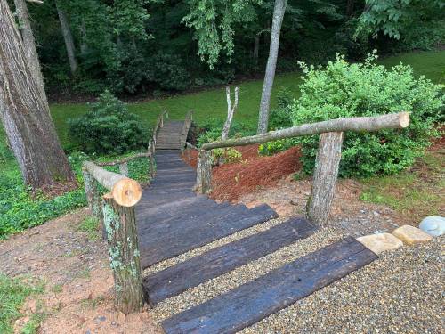 A wooden staircase leads down through a lush green forest, surrounded by trees and shrubs.